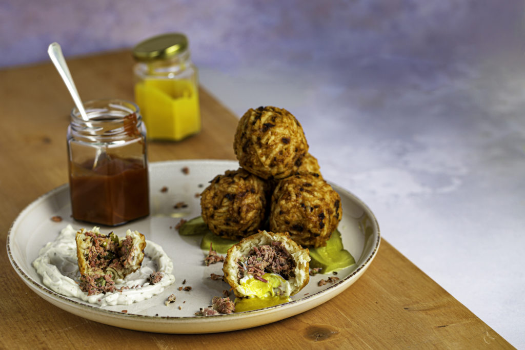 A plate of Latke Bonbons, with a side of ketchup and mustard. The bonbons are filled with salt beef